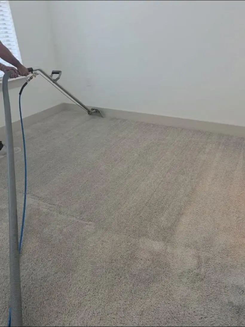 Technician running a steam-cleaning wand across beige carpet in an empty bedroom.
