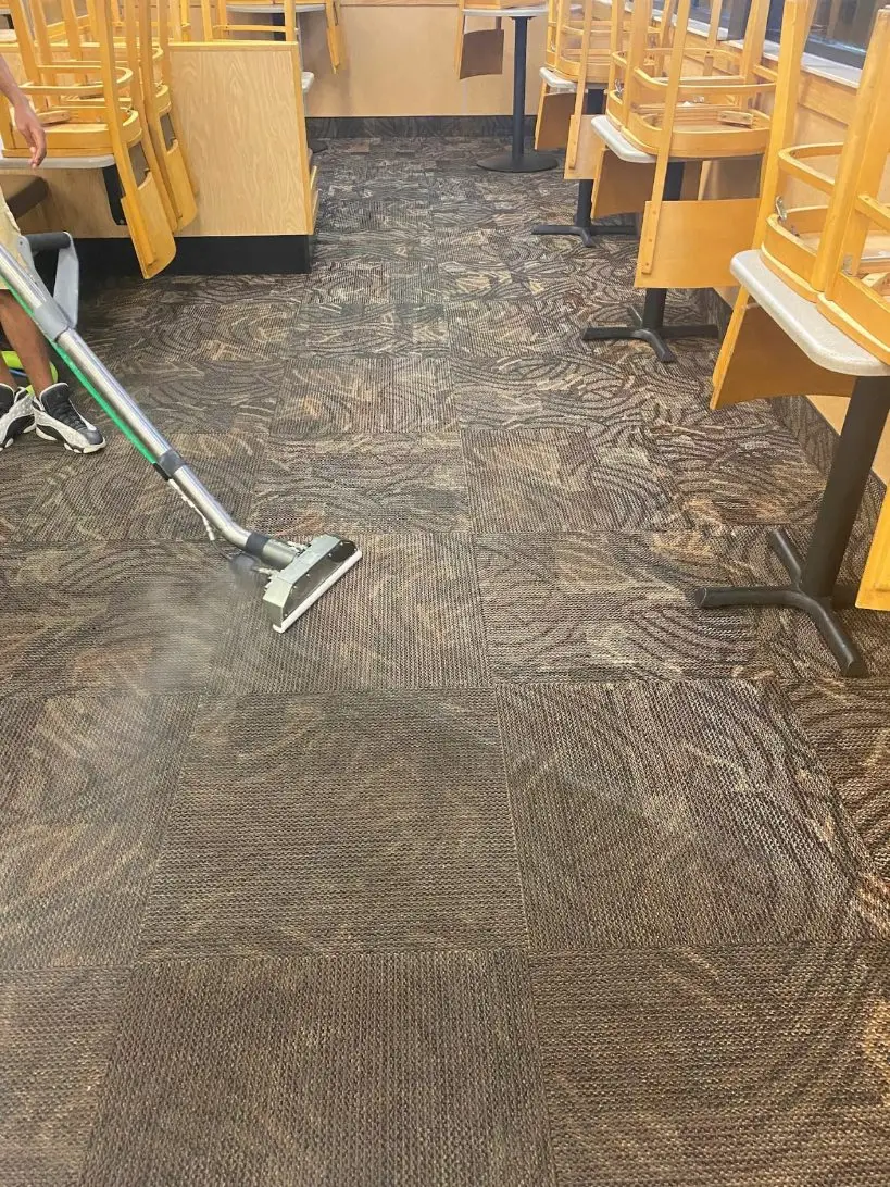 Steam cleaning patterned carpet tiles in a restaurant, chairs stacked on the tables.