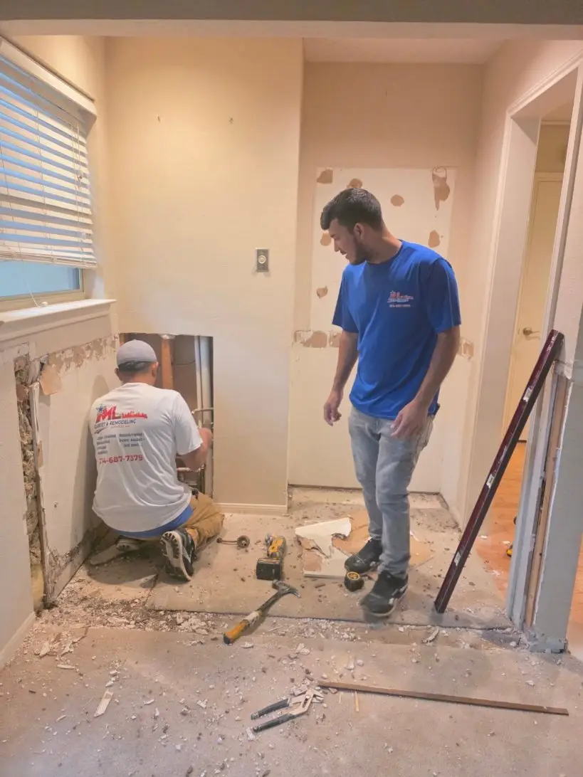 Two ML crew members at an opened wall, one kneeling at the plumbing and one in a blue ML shirt.