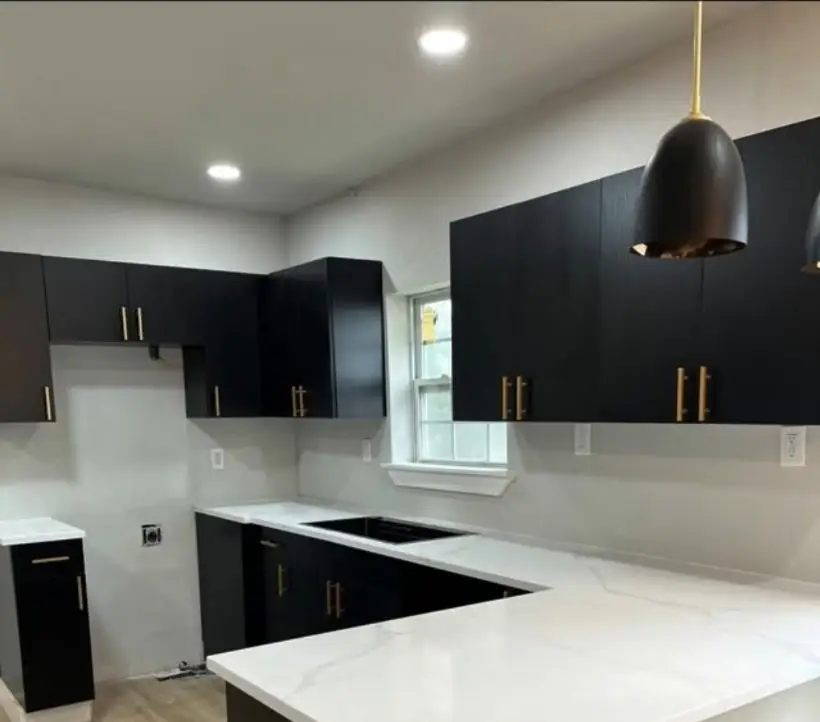 Kitchen with flat black cabinets, gold pulls and white quartz countertops.